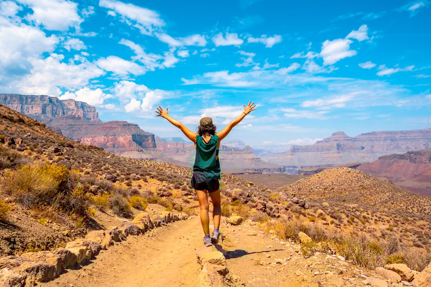 woman outside with arms raised to the sky with the grand canyon as a background