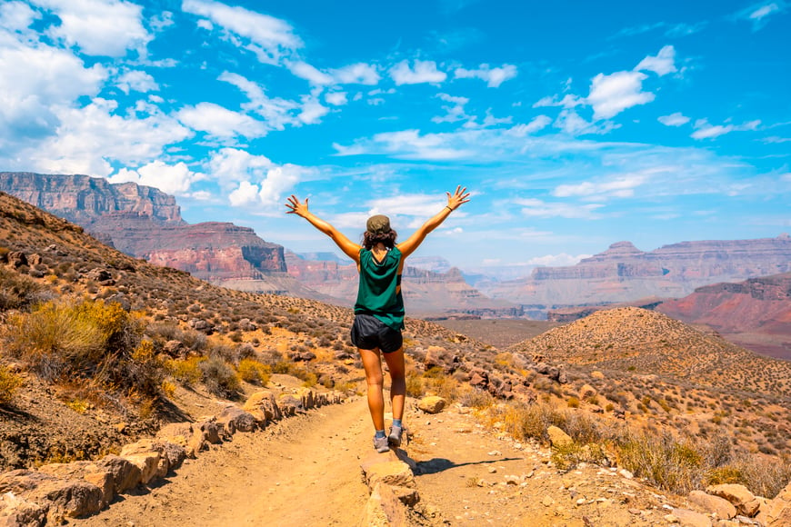 woman outside with arms raised to the sky with the grand canyon as a background