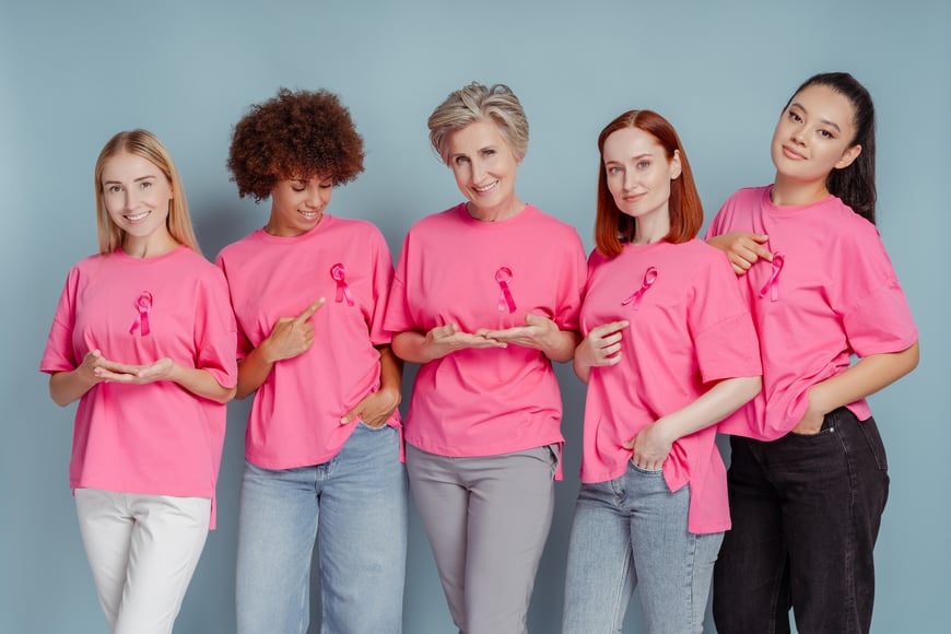 Five women wearing pink shirts and pink bows to raise awareness for breast cancer prevention. 