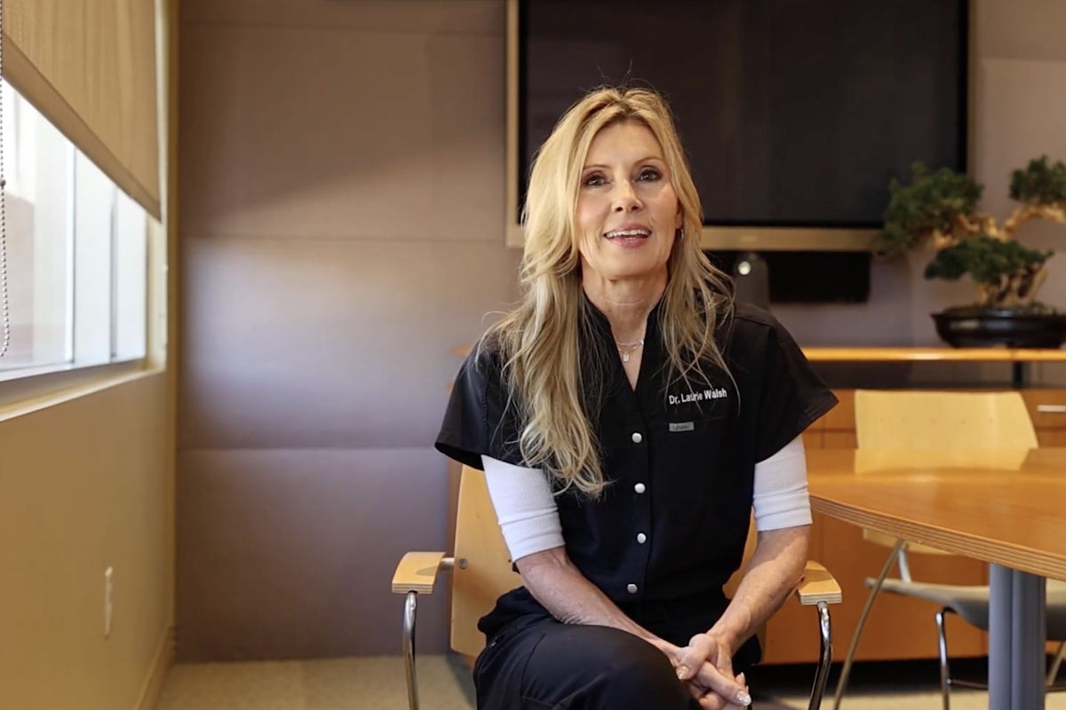 Dr. Laurie Walsh sits in a modern conference room, wearing black scrubs with a white undershirt.