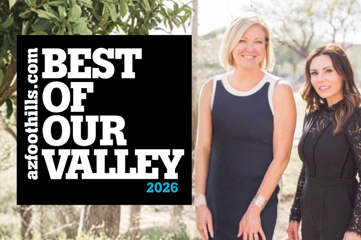 Two smiling women in dresses stand outdoors beside a large black banner that reads 'Best of Our Valley 2026'.