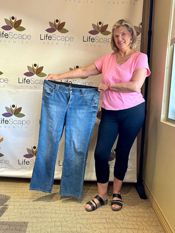 Smiling woman in a pink T-shirt holds up a pair of blue jeans in front of a LifeScape backdrop.