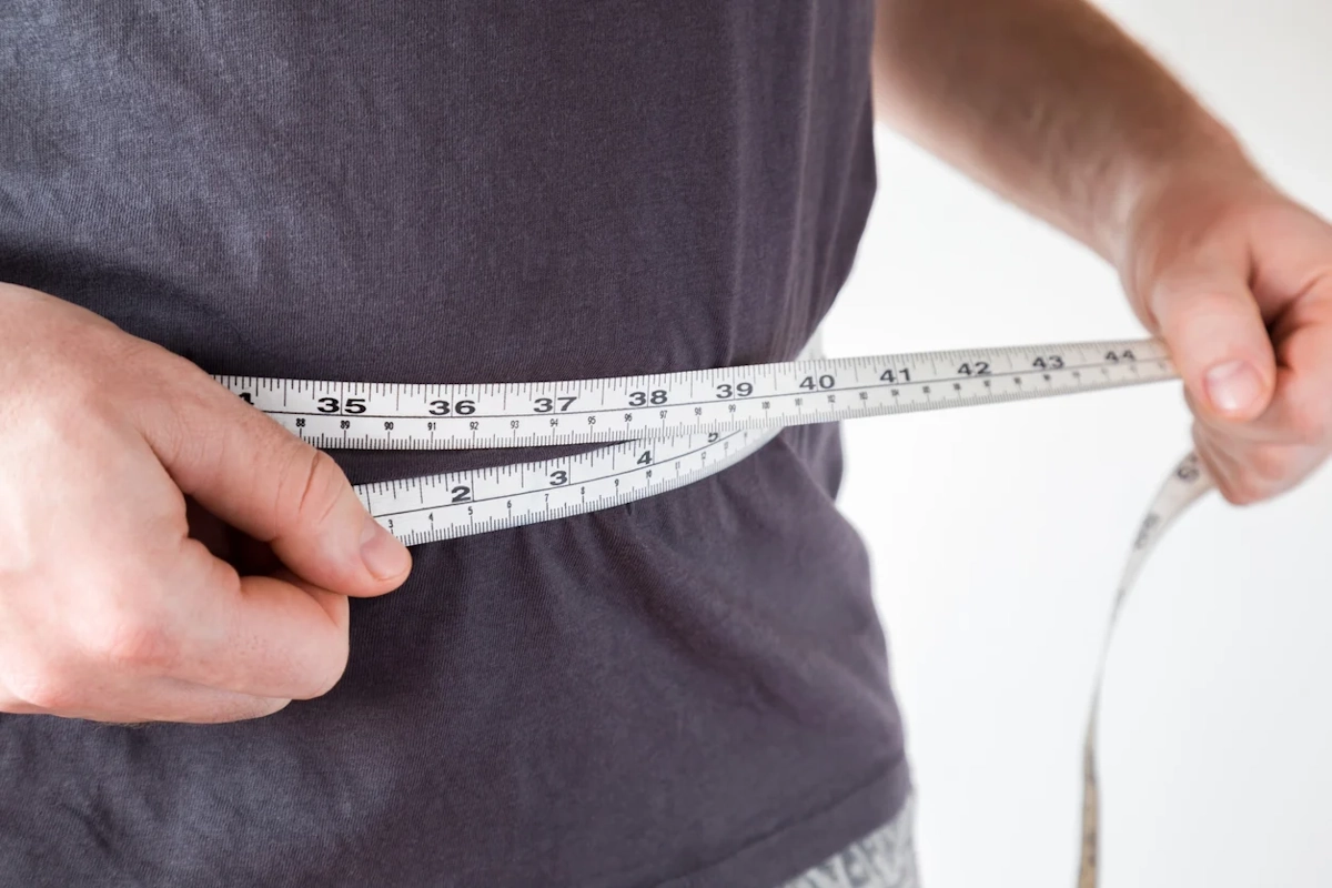 Person in a dark shirt wraps a measuring tape around their waist to take a measurement for fitness or tailoring purposes.