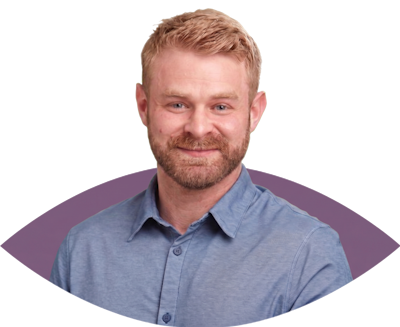 dr-lucas-no-bg - LifeScape Concierge Primary Care, Aesthetics & Nutrition in Scottsdale Smiling man with blond hair and a beard wearing a blue button-down shirt, against a purple curved backdrop.